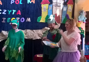 Na zdjęciu widać dwie nauczycielki i wolontariusza przebranego za smoka podczas imprezy " Cała Polska czyta dzieciom"